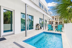 A modern house with a swimming pool, outdoor seating, and a view of neighboring buildings.
