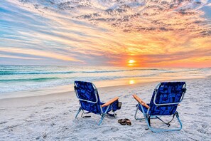 Zwei Strandstühle, die auf den Ozean ausgerichtet sind, mit einem Sonnenuntergang im Hintergrund.