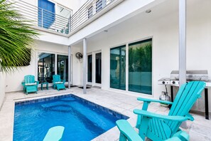 A modern outdoor pool area with a built-in grill and seating.