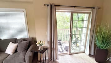 A living room with a sofa, a small table with a vase, a sliding glass door to an outdoor area, and a potted plant.