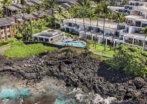 Et kysthotel med pool, omgivet af frodig vegetation og en klippefyldt kystlinje.
