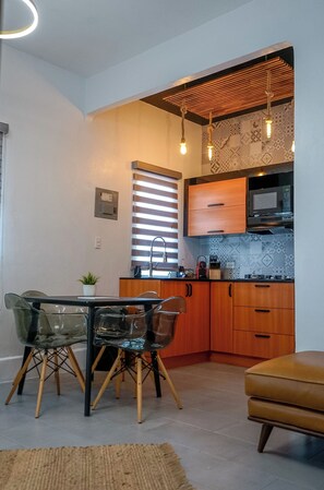 Cocina compacta con armarios de madera, microondas y comedor con mesa y sillas.