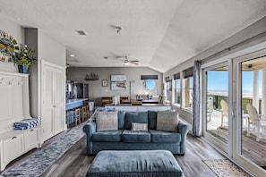 A spacious living area with a large window overlooking the beach, a kitchen in the background, and a cozy seating area with a blue sofa. - Galveston Beachfront Home with Gulf Views, Beach Access and Waterfront Deck (Galveston)