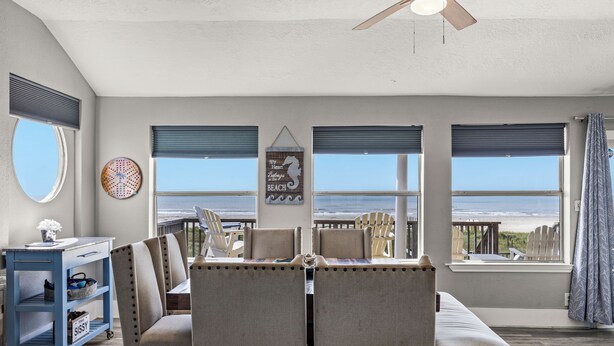 A dining area with a view of the beach, featuring a table with chairs, a ceiling fan, and a wall with a seahorse decoration. - Galveston Beachfront Home with Gulf Views, Beach Access and Waterfront Deck (Galveston)