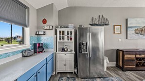 A kitchen with a stainless steel refrigerator, a coffee maker, and a window with a view of the outside. - Galveston Beachfront Home with Gulf Views, Beach Access and Waterfront Deck (Galveston)