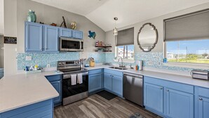 A modern kitchen with blue cabinets, stainless steel appliances, and a view of the outdoors. - Galveston Beachfront Home with Gulf Views, Beach Access and Waterfront Deck (Galveston)