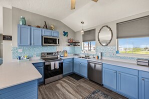Eine moderne Küche mit blauen Schränken, Edelstahlgeräten und Blick ins Freie.