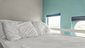 A bed with white bedding in a room with teal walls and a window with blinds. - Galveston Beachfront Home with Gulf Views, Beach Access and Waterfront Deck (Galveston)