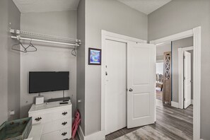 A room with a television, a white dresser, a door, and a hallway leading to another room. - Galveston Beachfront Home with Gulf Views, Beach Access and Waterfront Deck (Galveston)
