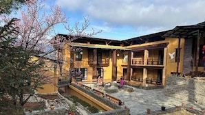 A courtyard with a building featuring a balcony and a stone wall. - Haven Resort Paro (Paro)