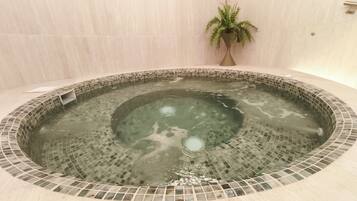 Un jacuzzi con detalles de mosaico, una planta en maceta y una pared revestida de azulejos.