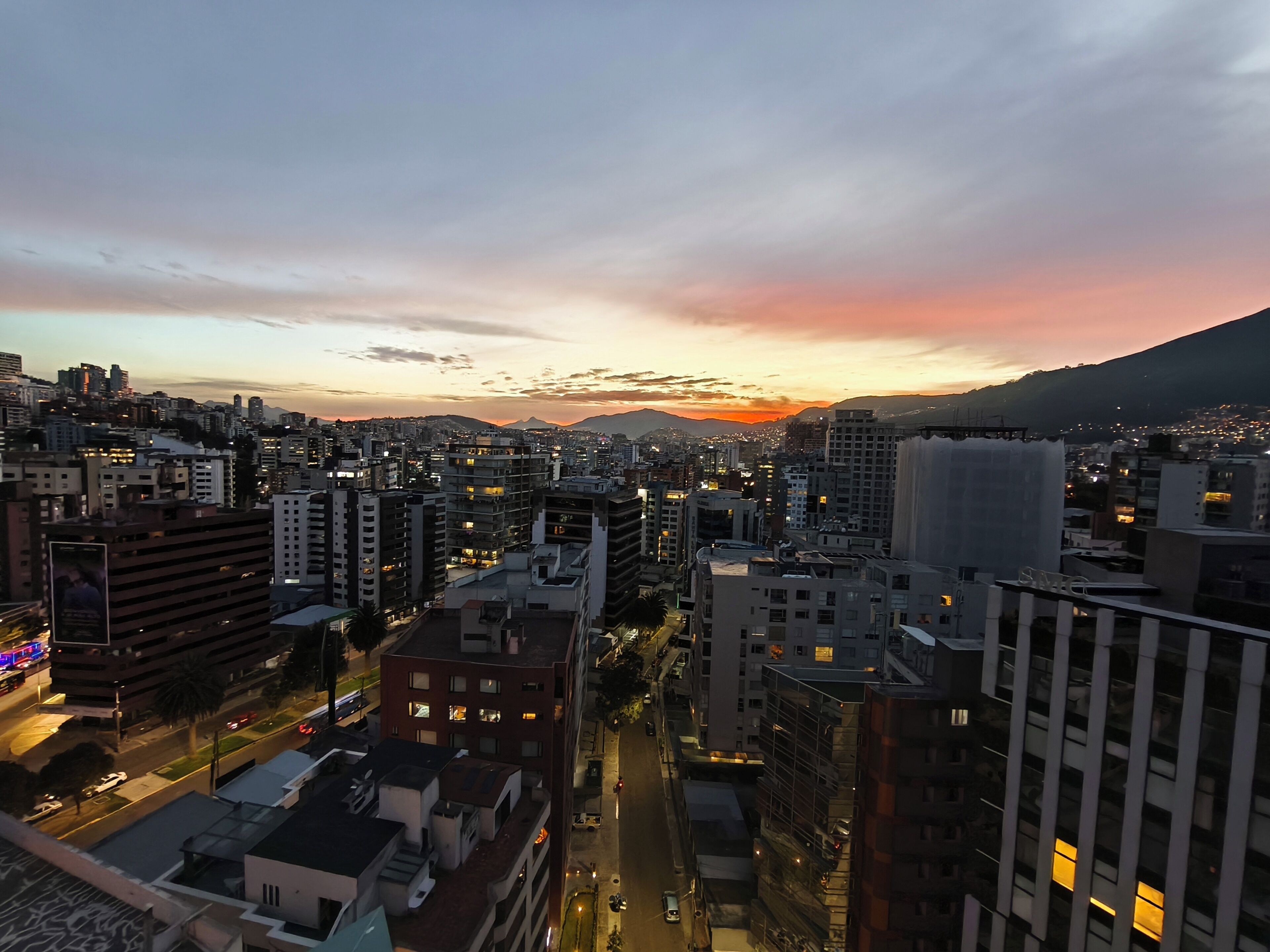 A cityscape at dusk with buildings and a mountain in the background.