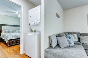 Una habitación con una cama, un electrodoméstico blanco, un sofá gris y un pequeño adorno en la pared.