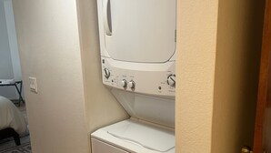 A compact laundry room with a washer and dryer, a wooden floor, and a door leading to another room. - Red Rock Memories - Pool / Spa / Pickleball (Sedona)