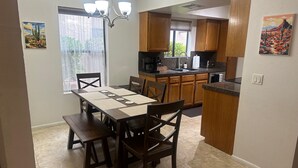 A dining area with a table set for four, wooden cabinets, a kitchen with a microwave, and a chandelier. - Red Rock Memories - Pool / Spa / Pickleball (Sedona)