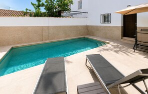 A rectangular swimming pool with two lounge chairs and a table, surrounded by a white wall with a tiled roof. - Gorgeous home in Iznajar (Iznajar)