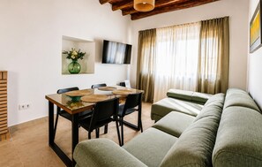 A living room with a sofa, a dining table with chairs, a flat-screen TV, and a window with curtains. - Gorgeous home in Iznajar (Iznajar)