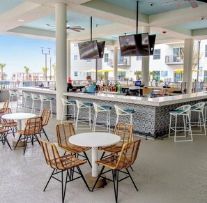 A bar area with white bar stools, a bar counter, and a television mounted on the ceiling. - Luxury 2b/2b Villa at New Oceanfront Resort – Pool, Beach & Balcony - Sleeps 8 (Myrtle Beach)
