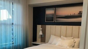 Una habitación de hotel con una cama, una mesita de noche, una lámpara y vista a la playa.
