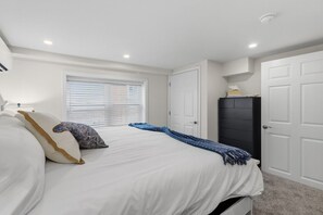 A bedroom with a bed, white walls, a window with blinds, a wardrobe, and a door. - North End 1BR/1BA Unit 4 - Walk to Beach & Boardwalk (Ocean City)