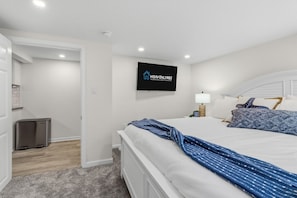 Ein Hotelzimmer mit einem Bett, einem an der Wand befestigten Fernseher, einem Mülleimer und einer Tür zu einem weiteren Raum.