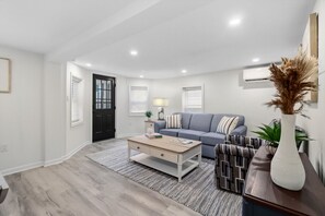 Ein modernes Wohnzimmer mit einem grauen Sofa, einem Holztisch und einem gemusterten Teppich.
