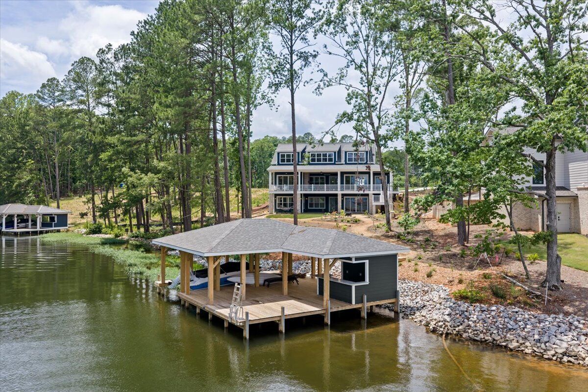 Une propriété au bord du lac, dotée d’un quai, d’un espace salon abrité et d’une grande maison avec de nombreuses fenêtres.
