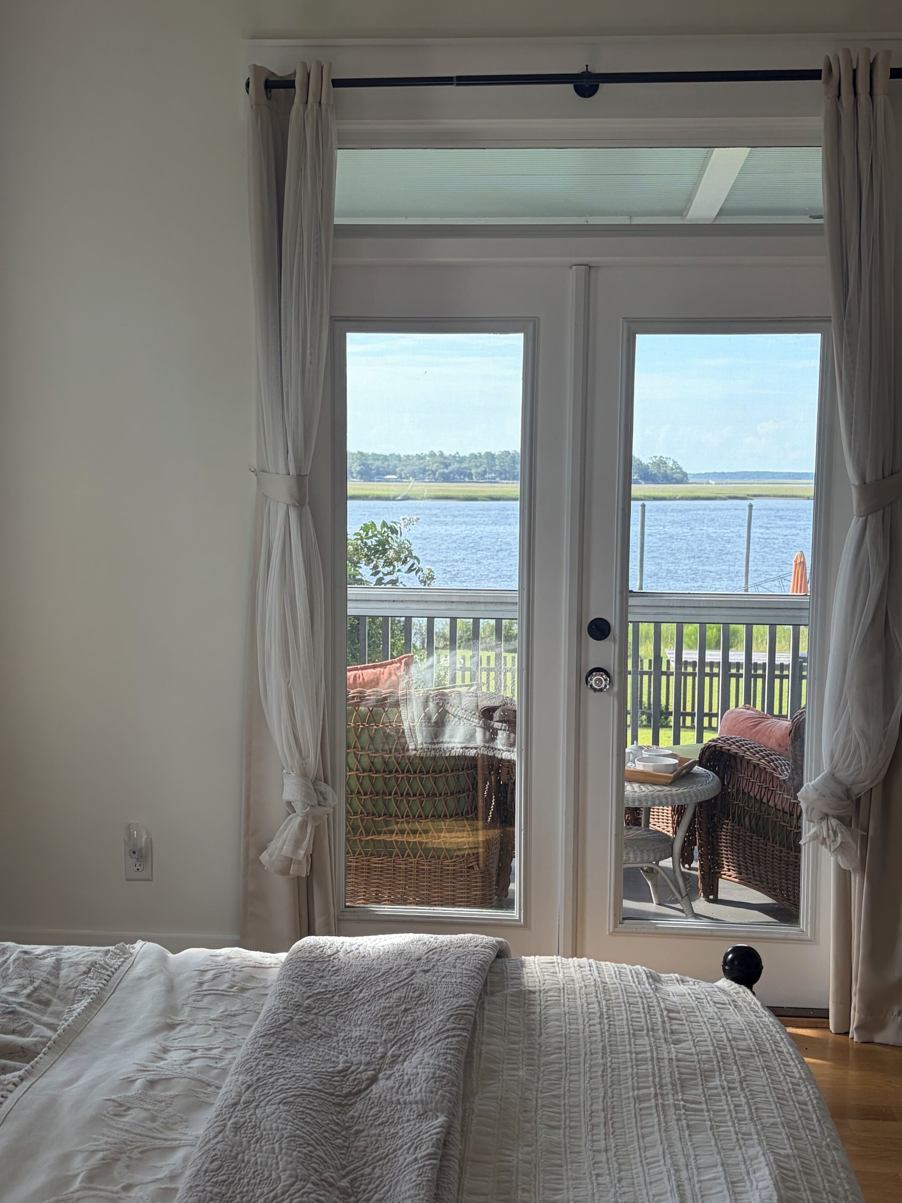Een slaapkamer met een groot bed, uitzicht op de omgeving door een schuifdeur en een balkon met tuinmeubilair.