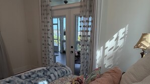 A bedroom with a bed, a window with curtains, a lamp, and a view of the outdoors. - DEEP WATER DOCK, PRIVATE POOL (Midway)