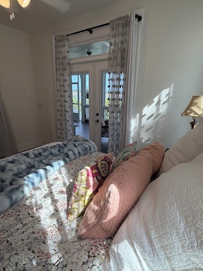 Ein Schlafzimmer mit einem Bett, einem Fenster mit Vorhängen, einer Lampe und Blick ins Freie.