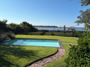 A swimming pool with a brick pathway leading to it, surrounded by a grassy lawn and a wooden fence. - DEEP WATER DOCK, PRIVATE POOL, two screened porches for dining and game watched. (Midway)