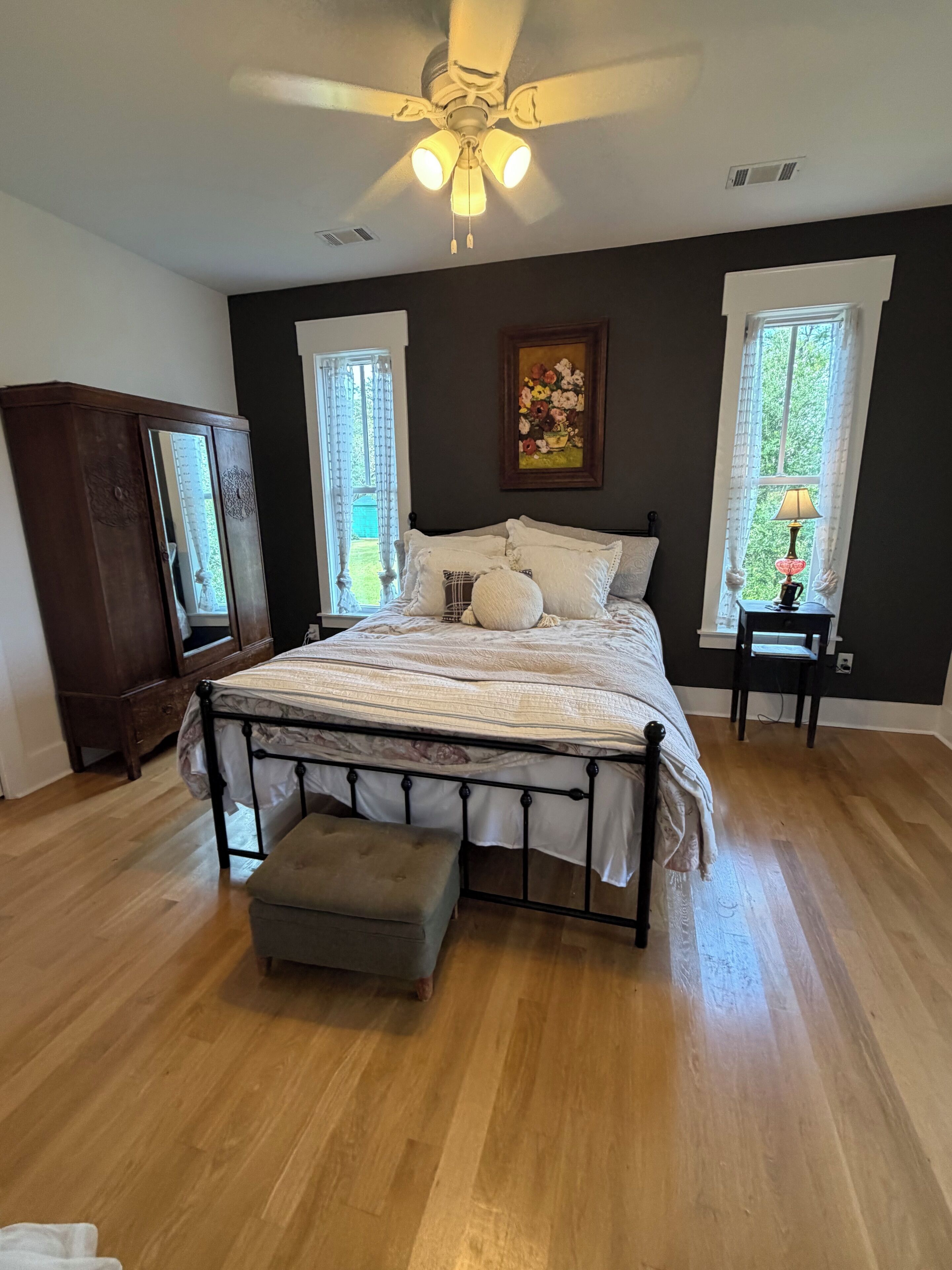 A bedroom with a bed, a nightstand, a lamp, a ceiling fan, and a window with curtains.