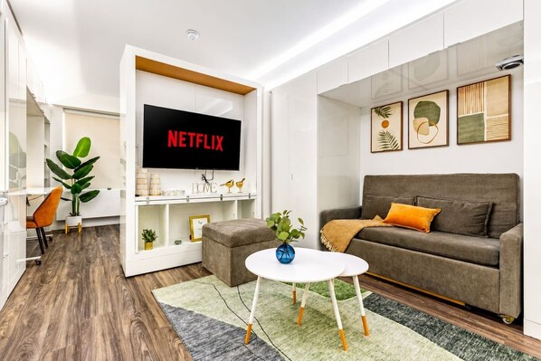 Een moderne woonkamer met een flatscreen televisie, een grijze bank, een salontafel en een plant.
