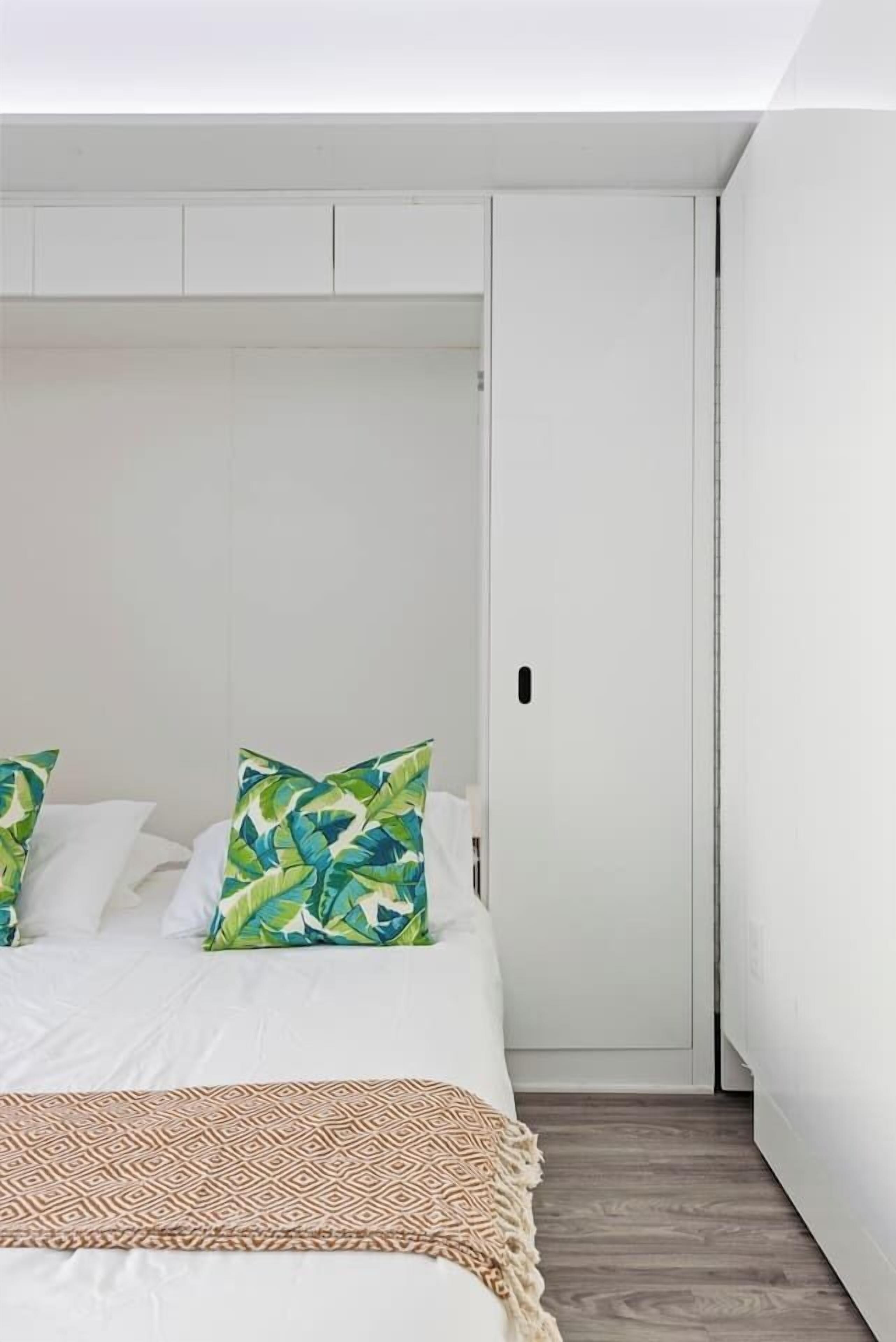 A bedroom with a bed, pillows, a blanket, and a wardrobe.