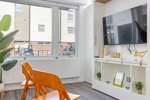 Ein Zimmer mit großem Fenster, einem Holzstuhl, einem Fernseher und einer Ablage mit Dekoration.