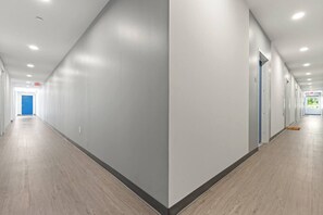 A long, narrow hallway with a blue door at the end, white walls, and wooden flooring.