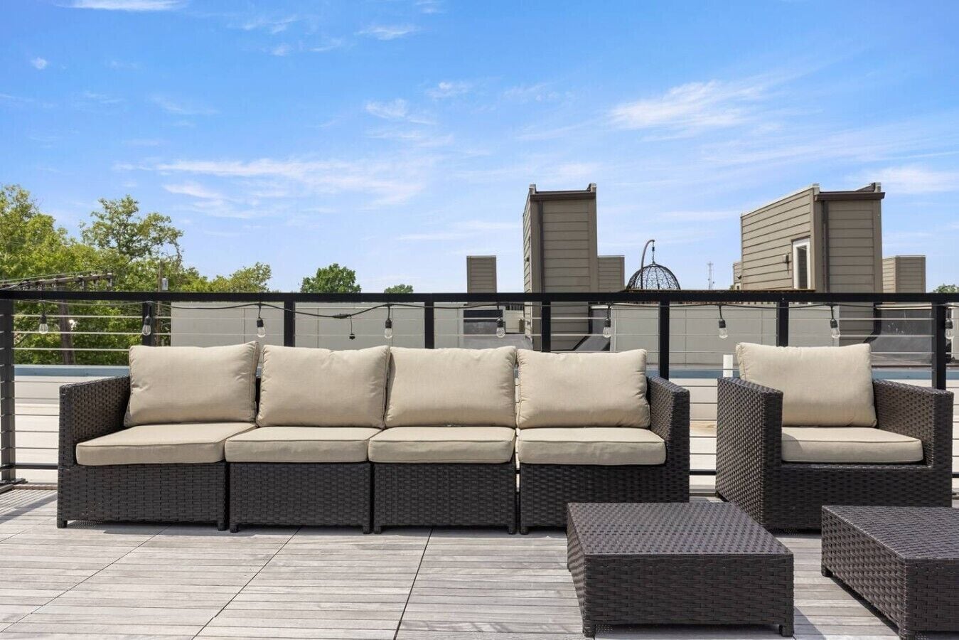 A rooftop patio with a dark wicker sofa set, a matching armchair, and a small table.