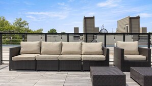 Eine Dachterrasse mit einer dunklen Rattan-Sitzgruppe, inklusive passendem Sessel und einem kleinen Tisch.