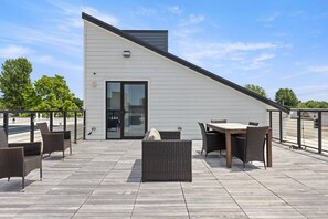 Een modern gebouw met een schuin dak, een glazen ingang en een terras met buitenmeubilair.