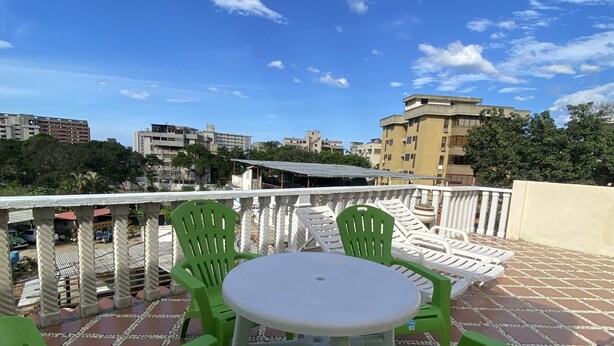 Eine Terrasse mit einem runden Tisch und grünen Stühlen, mit Blick auf eine Stadtlandschaft mit Gebäuden und Bäumen.
