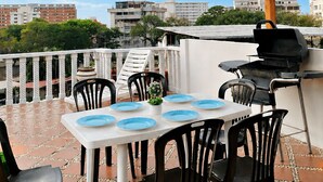 Eine Terrasse im Freien mit Tisch und Stühlen, einem Grill und Blick auf die Stadt.