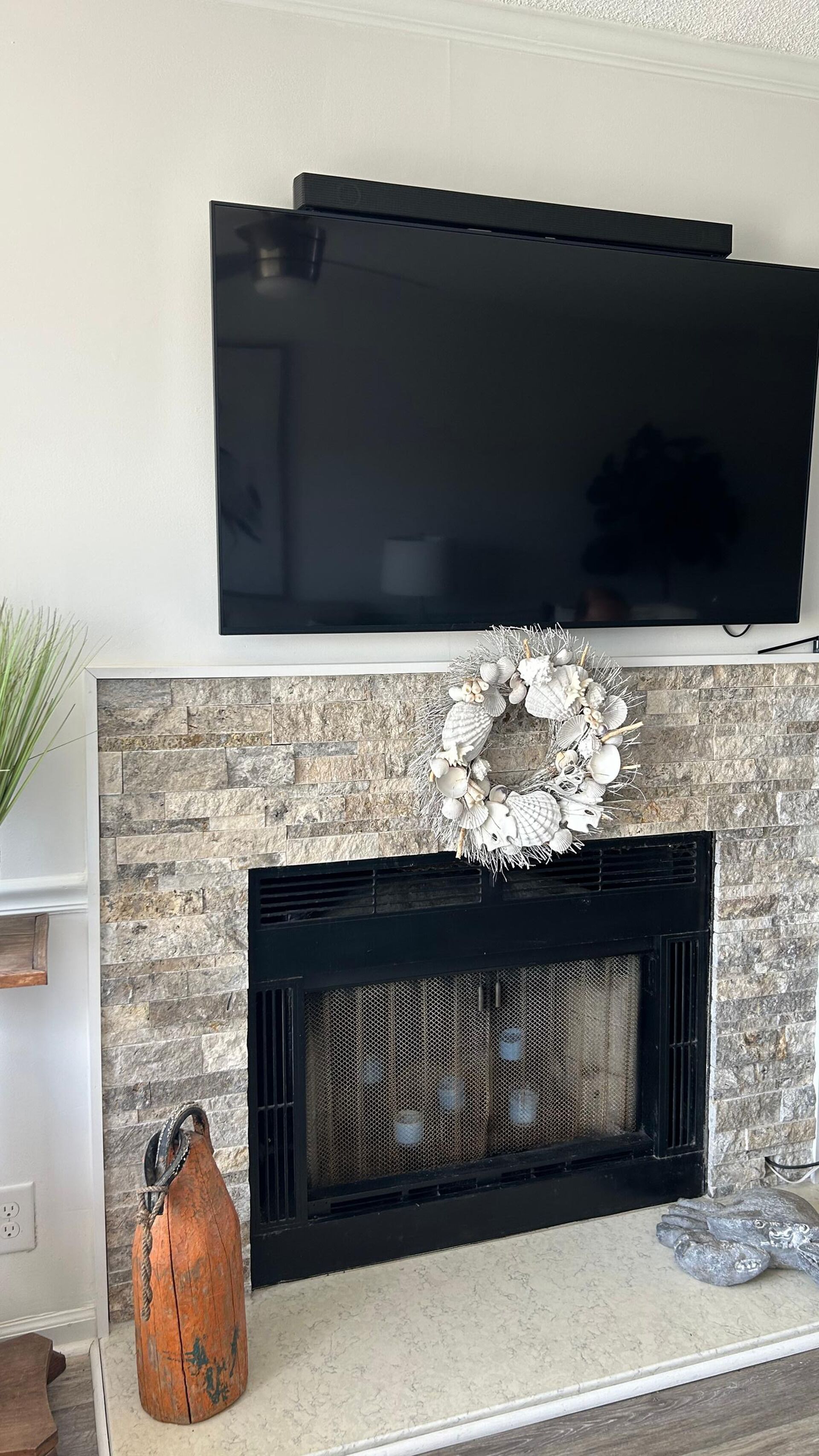 A flat-screen TV mounted above a fireplace with a decorative wreath.
