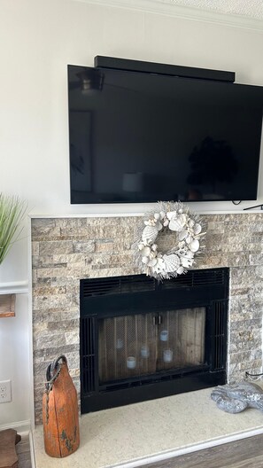 A flat-screen TV mounted above a fireplace with a decorative wreath. - Moss & Marsh | Marshfront Views, Pool & Island Charm (Saint Simons Island)