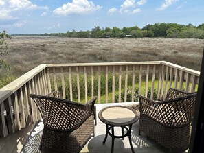 A wooden deck with wicker furniture and a view of a natural landscape. - Moss & Marsh | Marshfront Views, Pool & Island Charm (Saint Simons Island)
