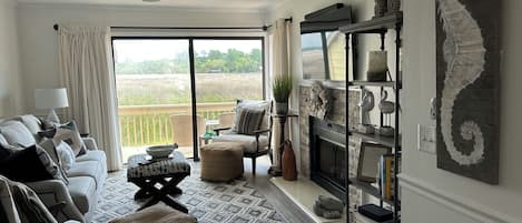 A living room with a sofa, ottoman, and a fireplace. There is a view of a field through the window.