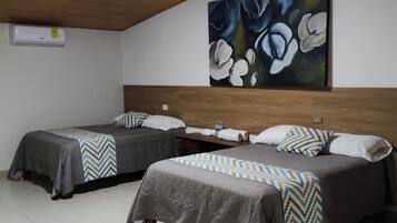 A hotel room with two beds, a wooden headboard, a painting of flowers, and a white air conditioning unit.