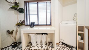 Une petite pièce propre, avec une fenêtre, un lave-linge blanc et une horloge au mur.