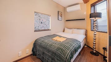 A bedroom with a bed, a wall-mounted air conditioner, a floor lamp, and a framed picture of Paris.