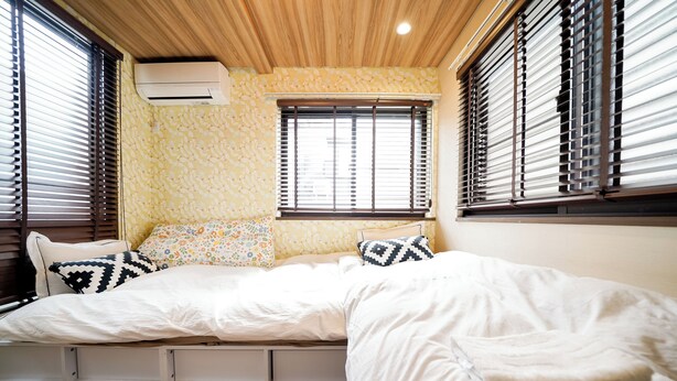 Une chambre à coucher avec un lit, deux fenêtres équipées de stores, un climatiseur et un mur décoré d’un motif.