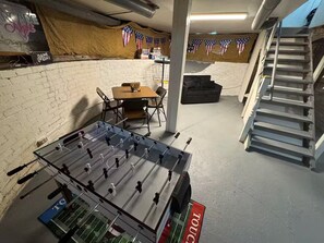 A room with a foosball table, a sofa, a table with chairs, and a staircase. - The All-Star Stay (South Bend)